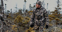Hunter wearing Pnuma cold weather gear with insulated jacket and pants, standing in a snowy forest, ready for late-season hunting.