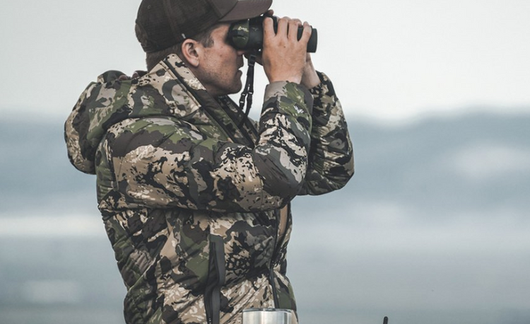 Man wearing camouflage hunting clothing, using binoculars to search for game