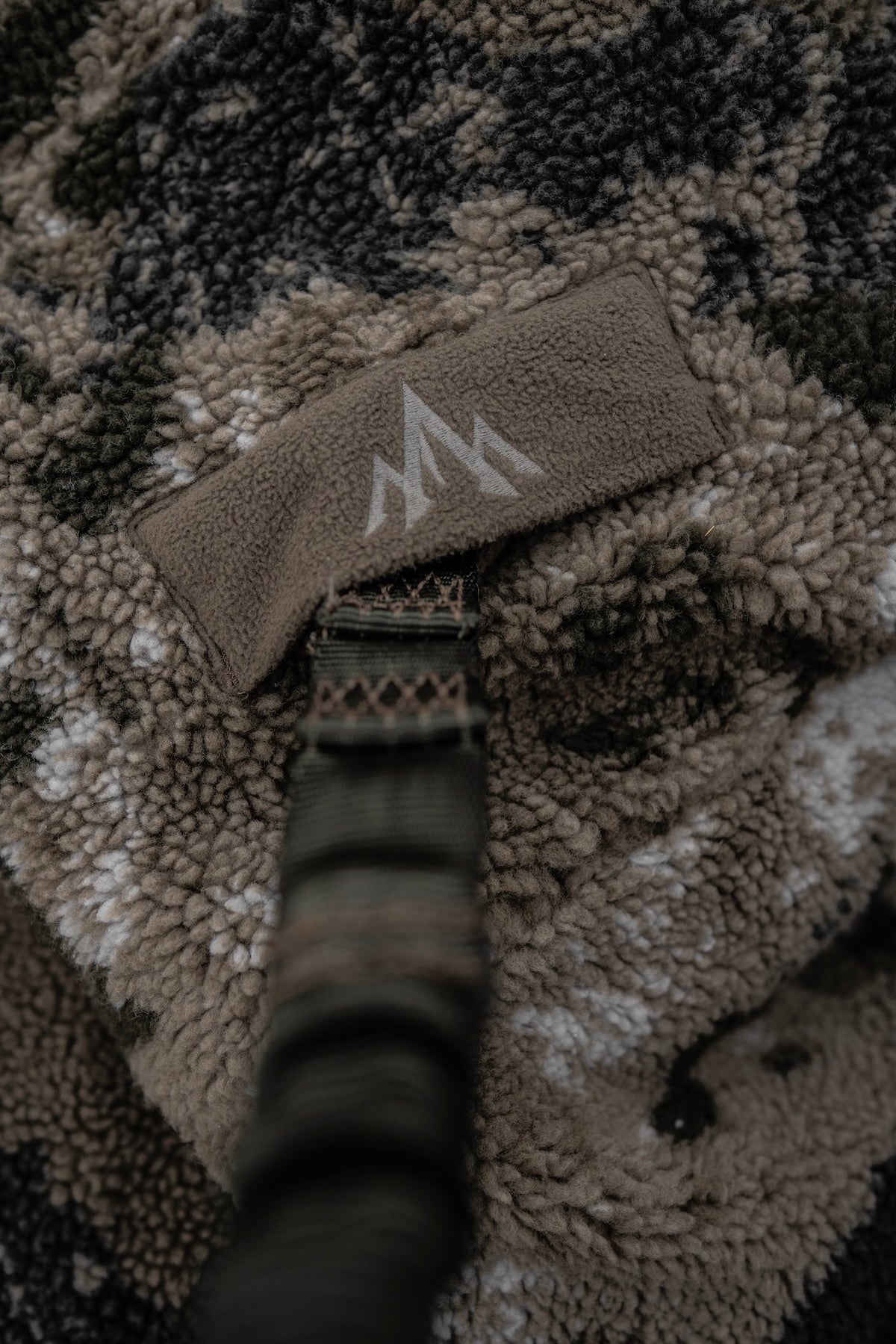 Close-up of the Pnuma Outdoors logo on a camouflage blanket, showcasing the mountain design against the fabric texture.