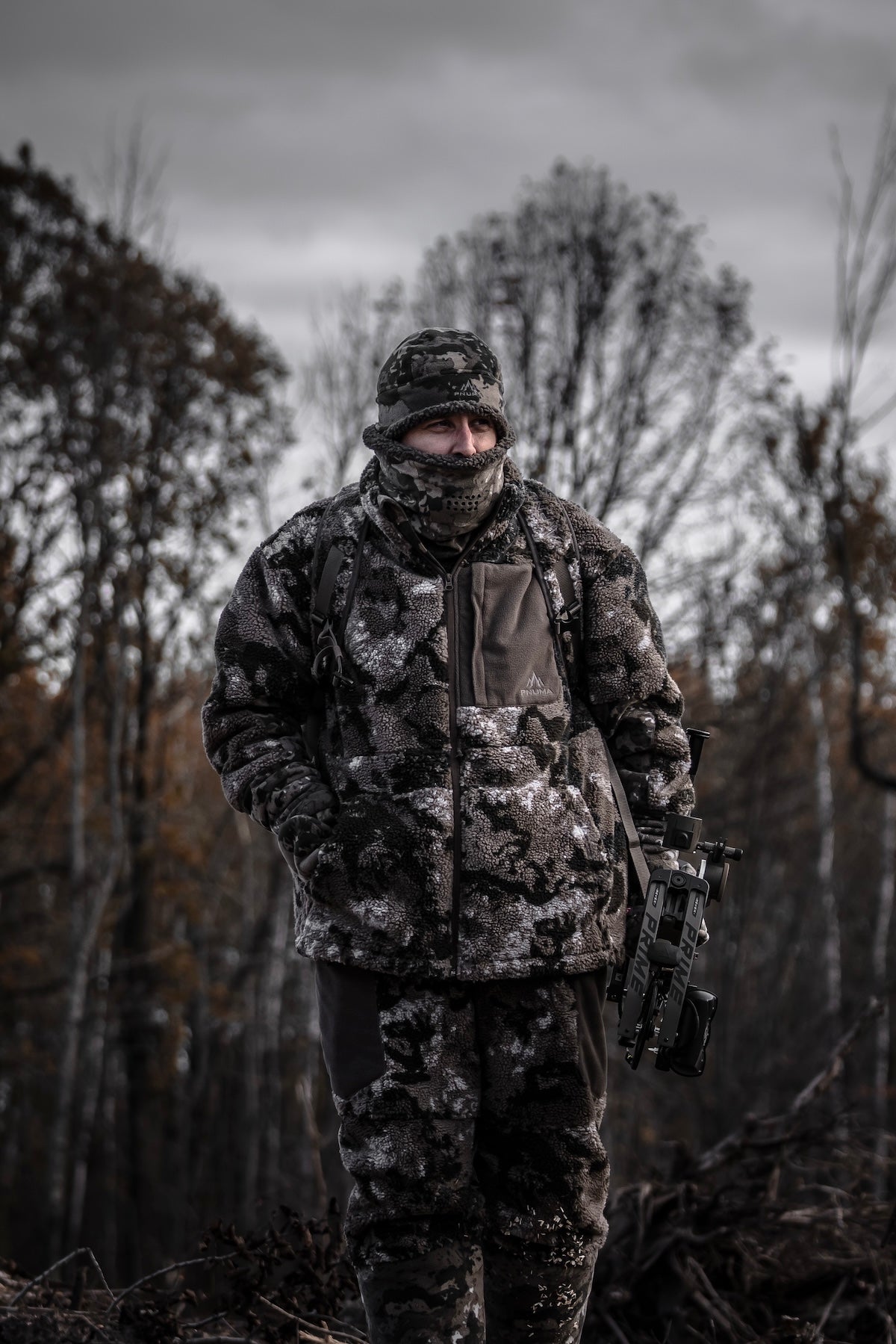 A man in camouflage winter wear stands in the woods, showcasing a Pnuma Outdoors product designed for hunters.