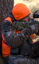 A man wearing a camouflage jacket from Pnuma Outdoor wear stands confidently against a natural backdrop.
