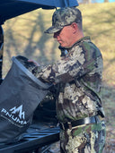 A man in camouflage is loading a bag into the back of a truck, showcasing outdoor gear from Pnuma Outdoors.