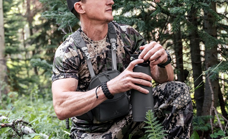Hunter wearing camouflage in the forest, opening a water bottle