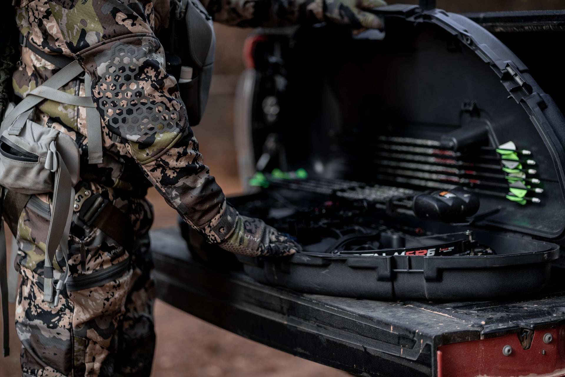 A man in camouflage gear stands holding a gun case, ready for an outdoor activity.